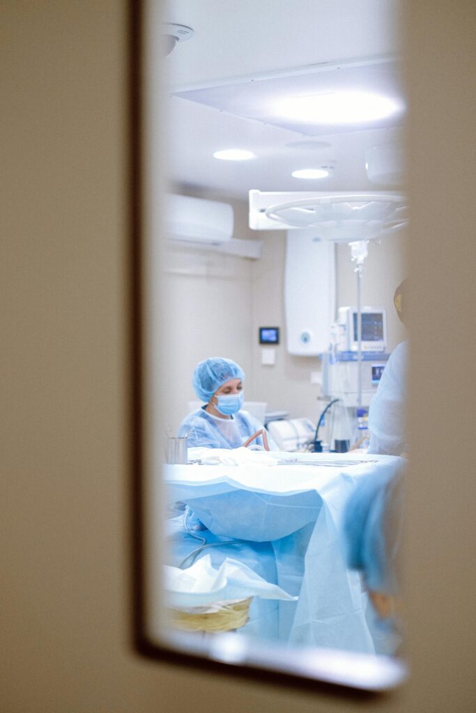 pexels-photo-4483323-4483323 View of a surgeon working in an operating room through a door window, emphasizing medical precision.